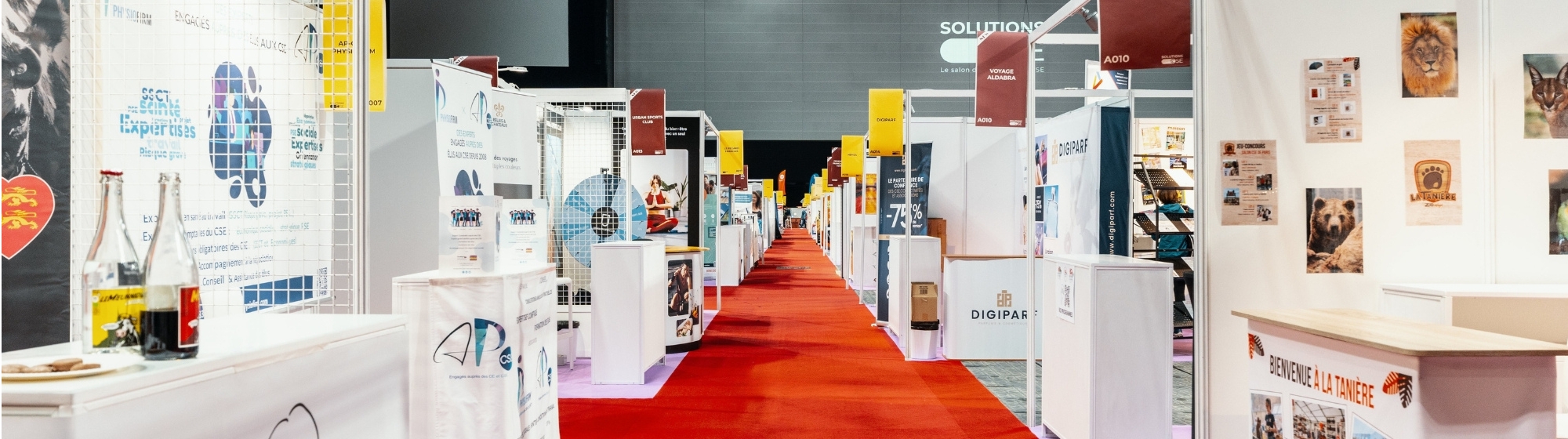 Allée centrale d’un salon avec les stands des exposants alignés de chaque côté.
