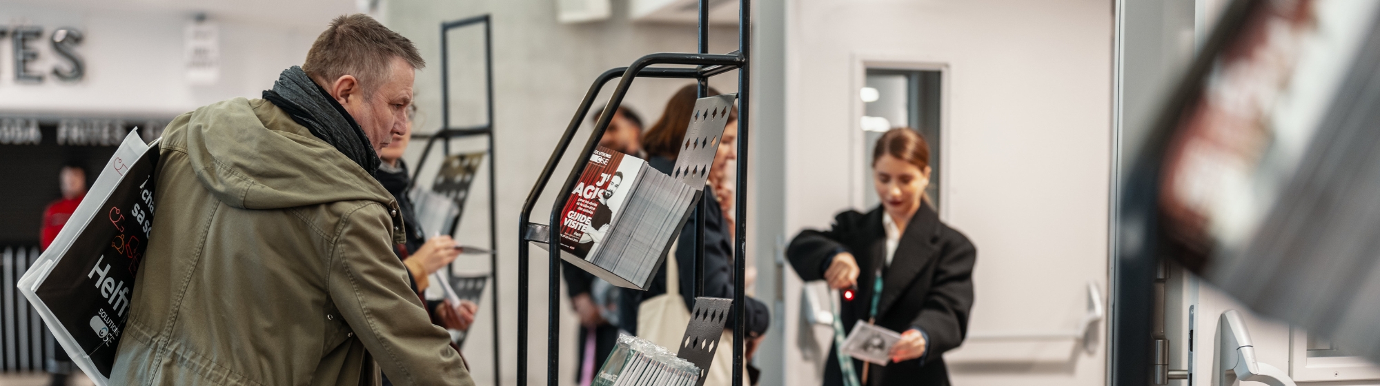 Visiteurs consultant un présentoir avec des guides de visite et informations pratiques lors d’un salon professionnel.