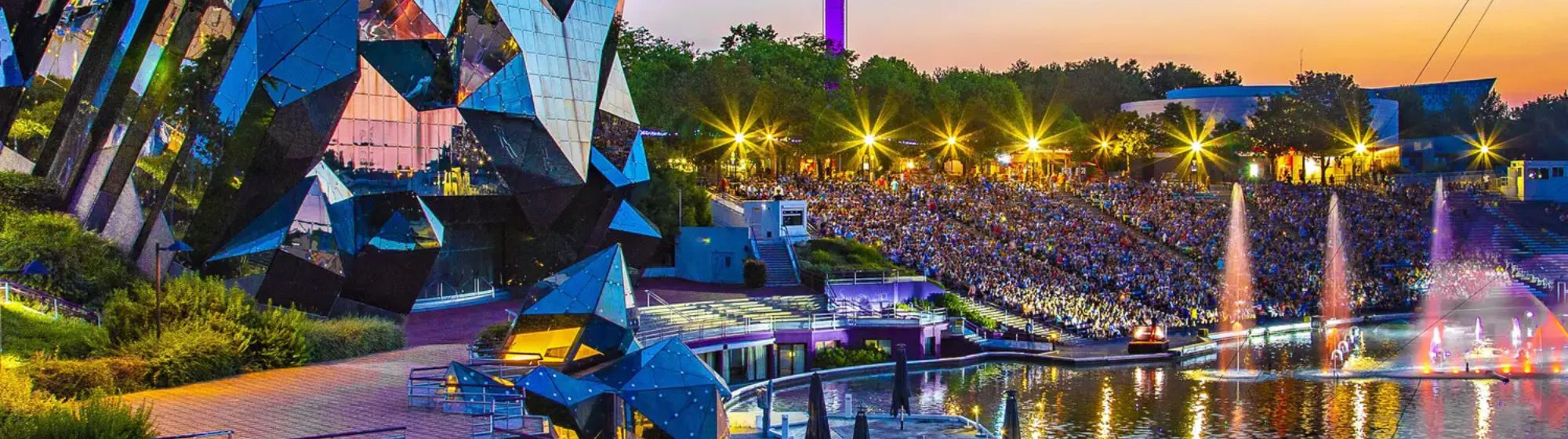 Vue nocturne du Futuroscope avec ses architectures futuristes, ses fontaines illuminées et son spectacle extérieur