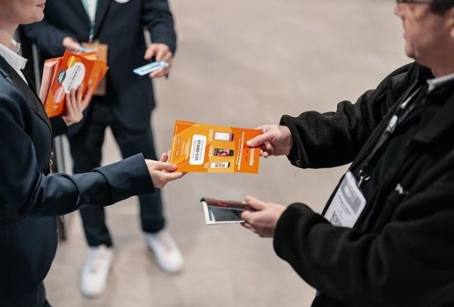 Une femme tendant un flyer orange à un homme