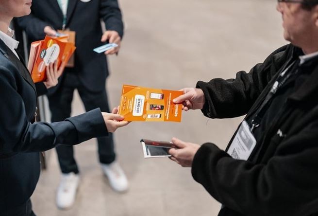 Une femme tendant un flyer orange à un homme
