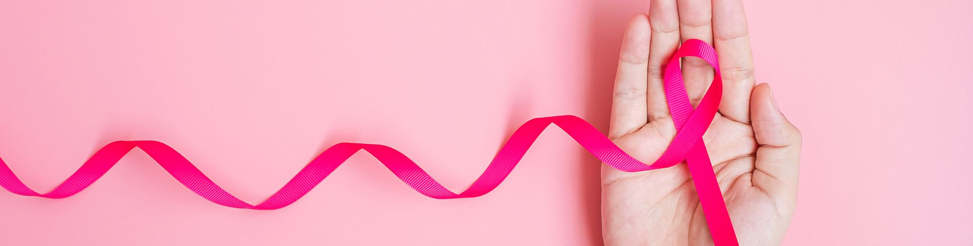 Prévention : le ruban rose au cœur de la sensibilisation Main tenant un long ruban rose sur fond rose, symbole de sensibilisation à la prévention.