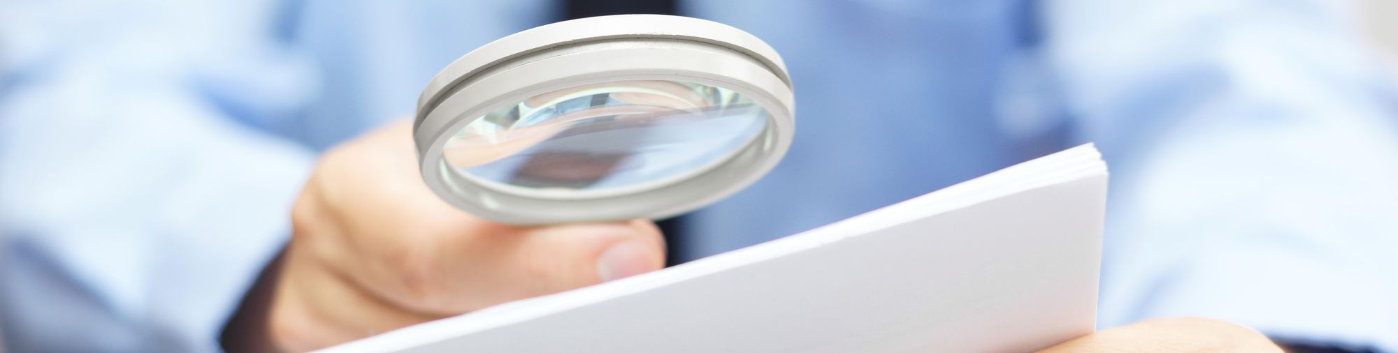 Personne consultant un document avec une loupe pour illustrer les contrôles et obligations URSSAF