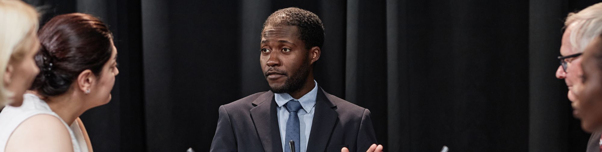 Homme en costume prenant la parole devant plusieurs participants lors d’un échange professionnel.