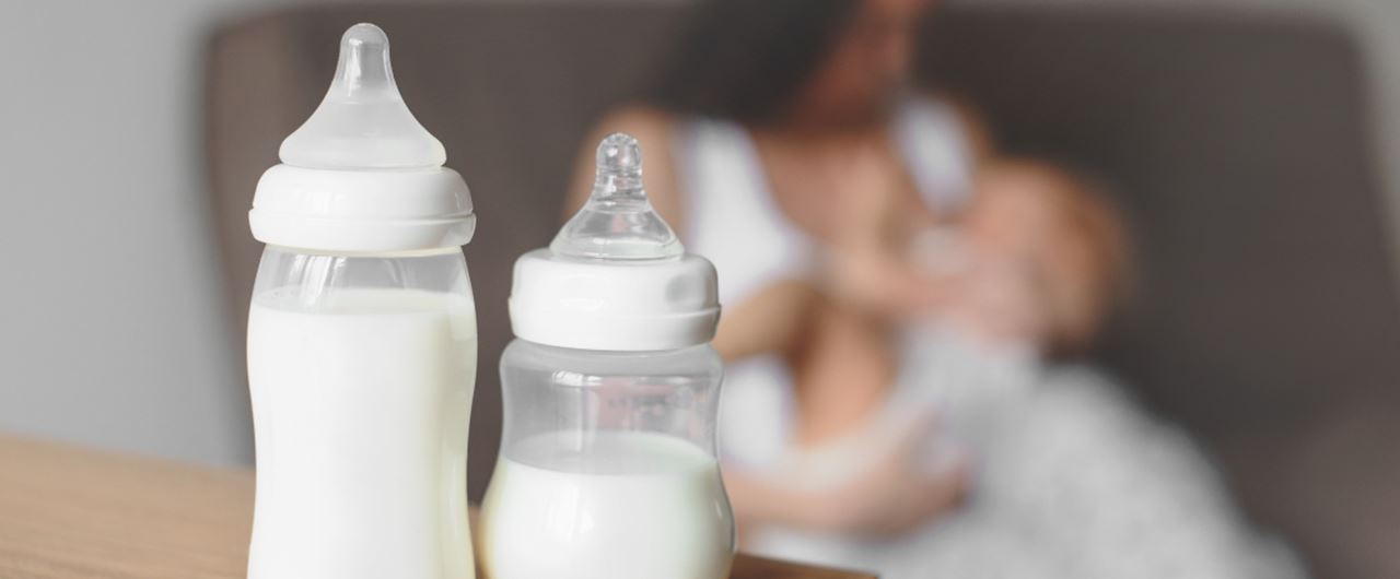 Deux biberons posés sur un table avec une femme et un bébé derrière