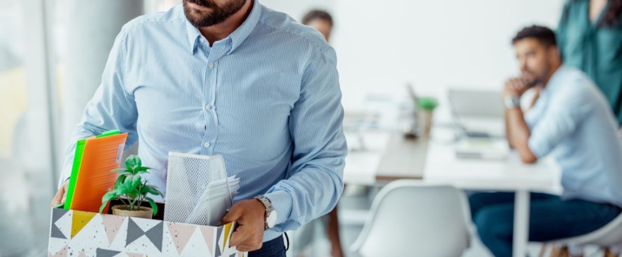 Un homme s'léoignant avec un carton rempli de ses affaires