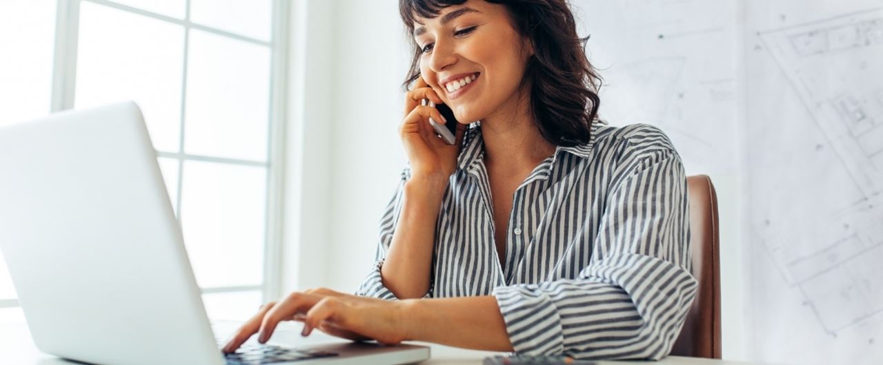 Jeune femme face à un ordinateur et un téléphone à l'oreille