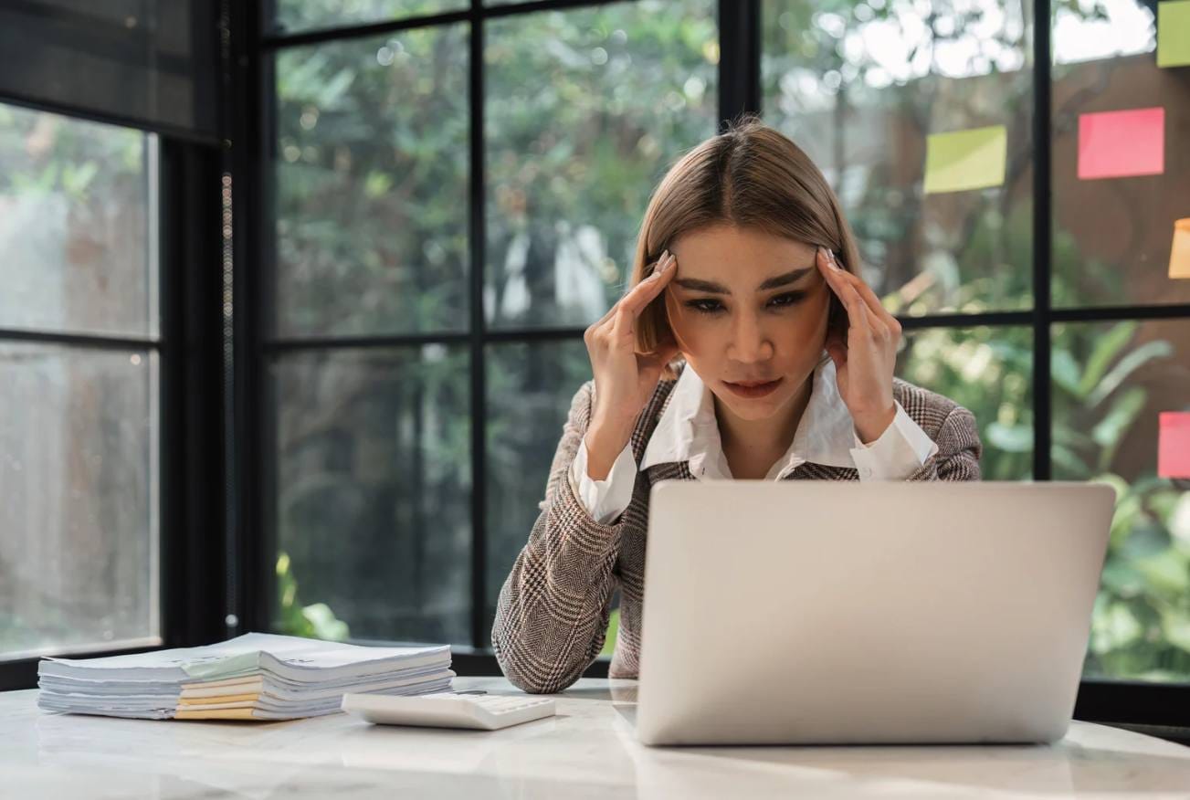 Une femme se tenant la tête devant un ordinateur