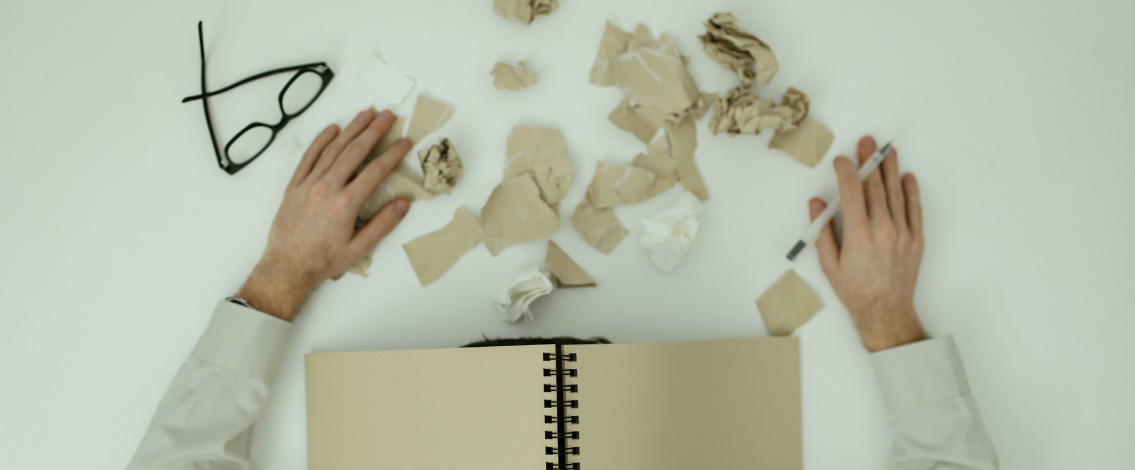 Un homme avec les bras posés sur une table avec un cahier retourné