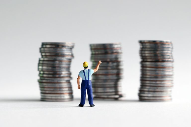 Trois piles de monnaies avec un ouvrier miniature devant