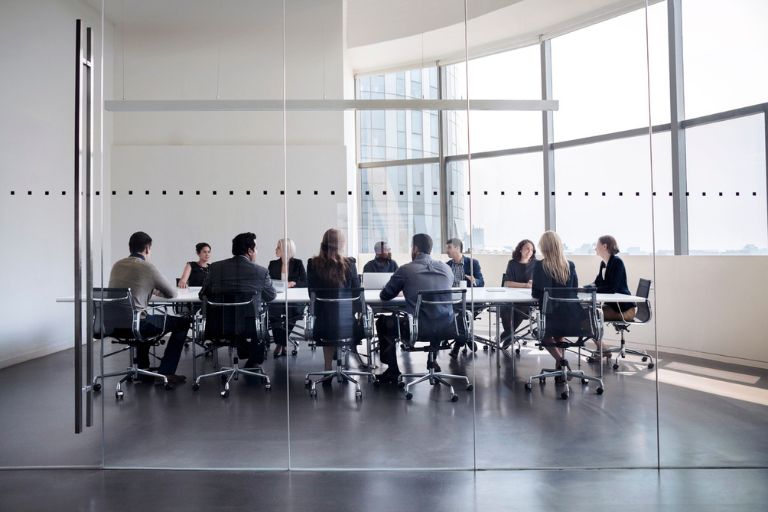 Salle de réunion avec plusieurs personnes assises autour d'une tablz