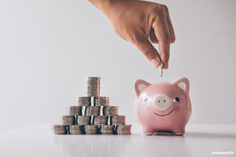 Une personne mettant une pièce de monnaie dans une tirelire à côté de pièces de monnaies