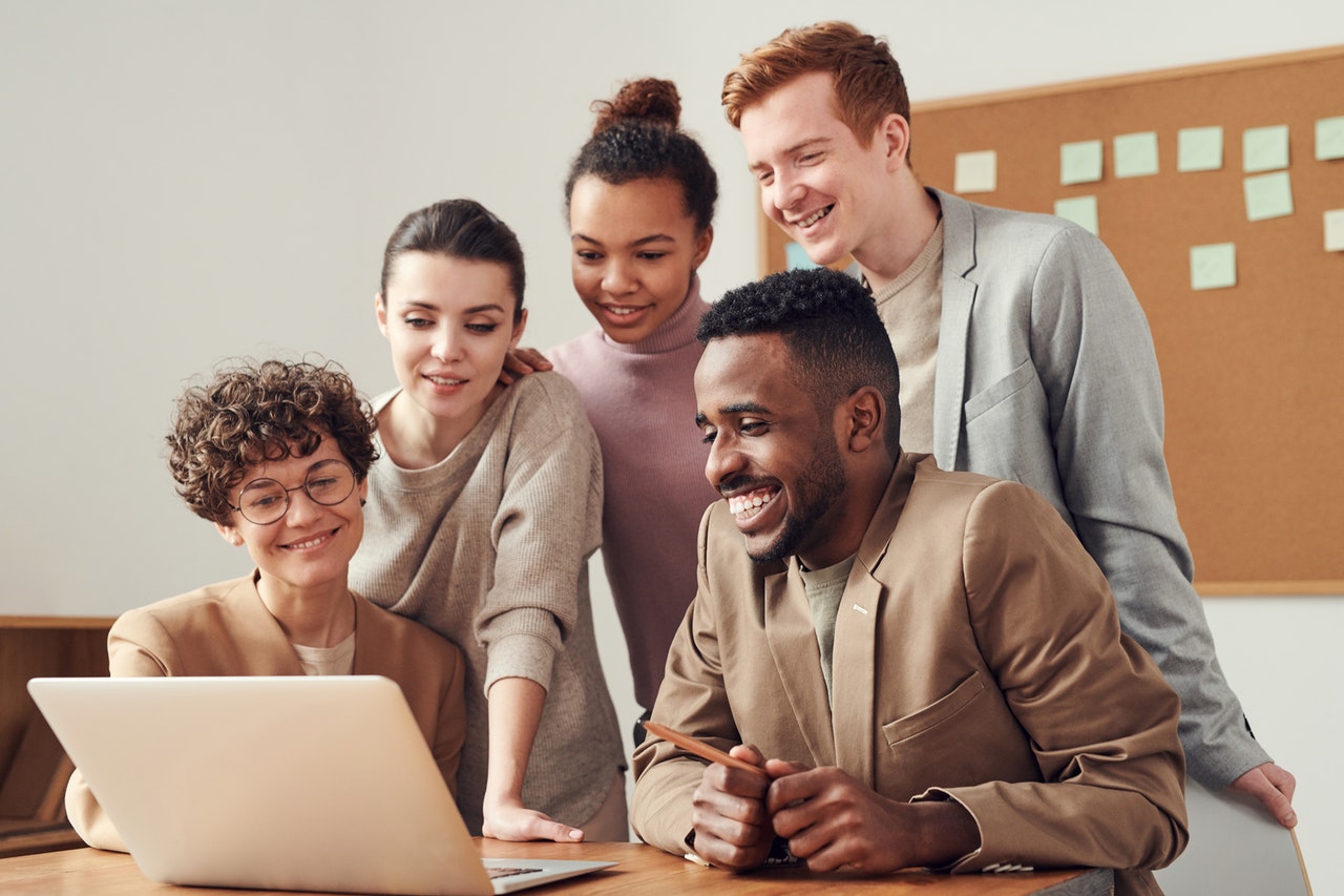 Cinq jeunes personnes souriant devant un tableau en liège