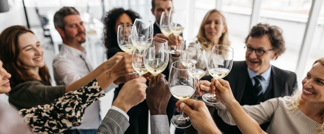 Groupe de collègues célébrant et trinquant avec des verres de vin blanc lors d’une réunion professionnelle.
