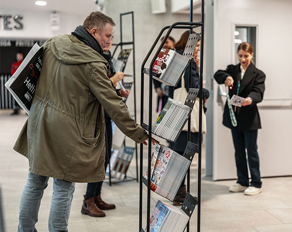 Photographie mettant en avant une jeune fille scannant un QR Code, et un homme regardant les documents mis à disposition sur un présentoir
