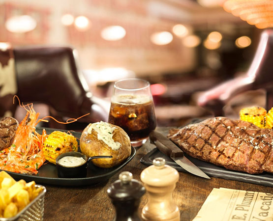 Photographie d'une table de restaurant dressée, avec deux plats contenant des pommes de terre, du maïs et de la viande