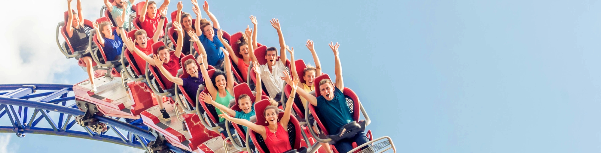 Personnes criant et levant les bras sur un grand huit en parc d’attractions