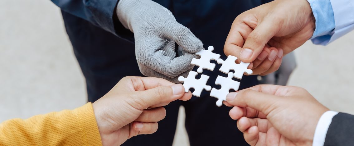 Quatre mains assemblent des pièces de puzzle blanches symbolisant collaboration et union